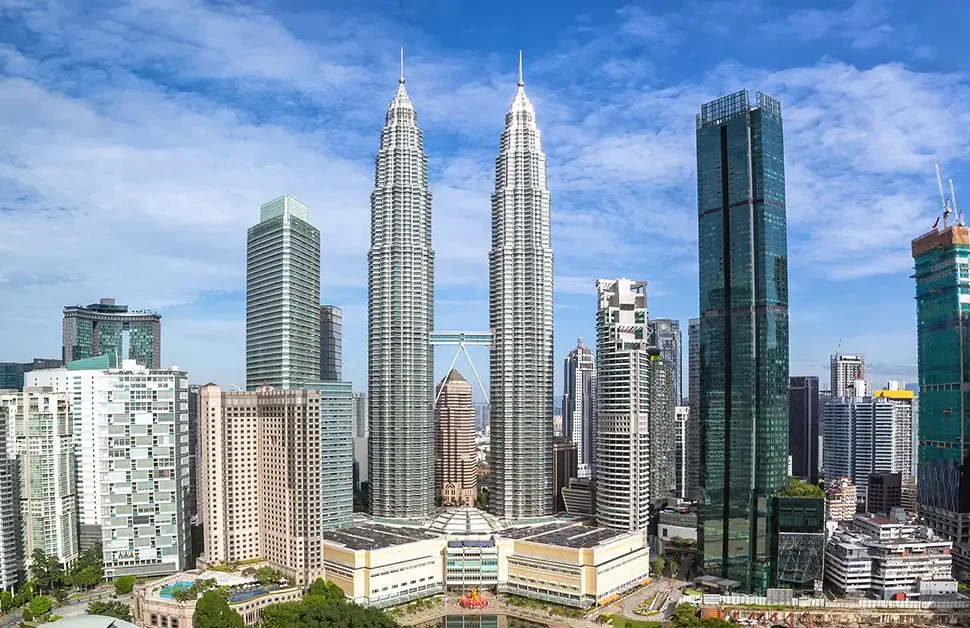 A panoramic view of Kuala Lumpur city featuring the iconic Petronas Twin Towers under a blue sky.